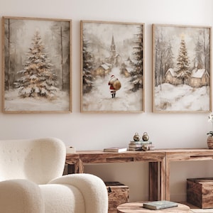 May include: Three framed winter landscape paintings depicting a snowy village, a Christmas tree, and Santa Claus walking through the snow. The paintings are hung on a white wall above a wooden table with a white armchair and a round wooden coffee table.