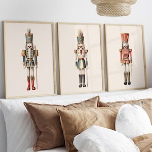 May include: Three framed prints of vintage-style illustrations of nutcracker soldiers. The nutcrackers are wearing different colored uniforms, including blue, green, and red. The prints are displayed on a white headboard with brown pillows.