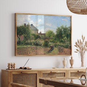 Könnte beinhalten: Ein gerahmtes Gemälde einer Gartenszene mit einem Haus im Hintergrund. Das Gemälde hängt an einer weißen Wand über einem Holzschrank mit geflochtenen Rattan-Türen. Auf dem Schrank stehen Pflanzen und eine Vase mit getrockneten Blumen.