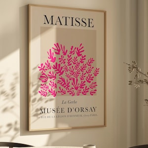 May include: A framed art print featuring the word "MATISSE" at the top, with a pink floral design below. The text "MUS&Eacute;E D'ORSAY" is at the bottom. The print is in a light wood frame and hangs on a white wall.