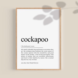 May include: A framed print with the word "cockapoo" in a large, black font. The definition of cockapoo is below the word. The print is in a light wooden frame, with a neutral background.