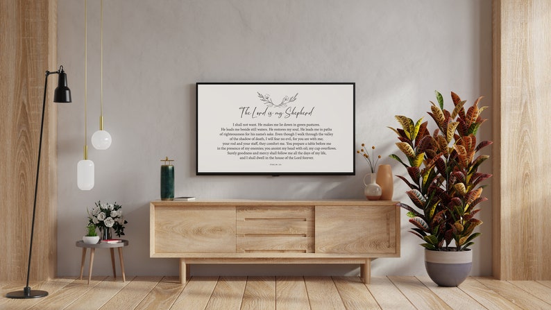 Puede incluir: Un mueble de TV de madera con un televisor de pantalla plana que muestra una impresi&oacute;n en blanco y negro del Salmo 23, "El Se&ntilde;or es mi pastor". El televisor est&aacute; en un sal&oacute;n con una planta en maceta, una l&aacute;mpara de pie y una mesita auxiliar.