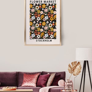 May include: A framed print with a floral pattern in shades of yellow, orange, pink, and blue on a black background. The print has the text "FLOWER MARKET" and "STOCKHOLM" in white.