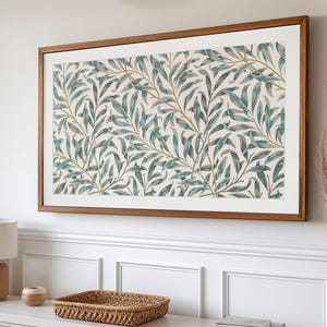 May include: A framed art print featuring a botanical pattern of blue-green leaves and gold stems on a cream background. The artwork is displayed in a rectangular, wooden frame, mounted on a white wall.