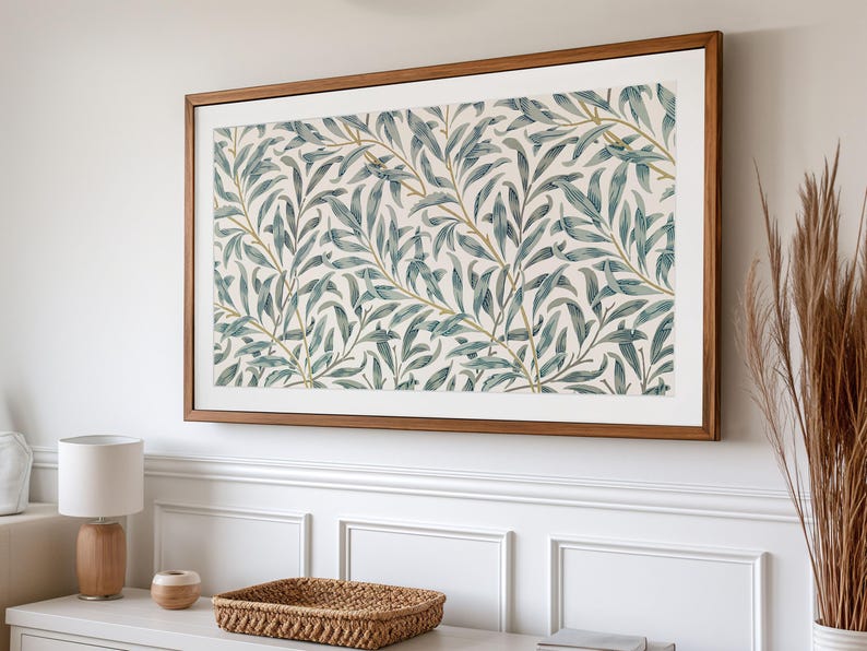 May include: A framed art print featuring a botanical pattern of blue-green leaves and gold stems on a cream background. The artwork is displayed in a rectangular, wooden frame, mounted on a white wall.