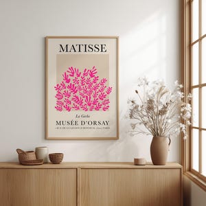 May include: A framed art print featuring a pink floral design against a beige background, with the name "MATISSE" at the top. Below, the text reads "MUS&Eacute;E D'ORSAY, Paris". The print is displayed on a wooden cabinet.