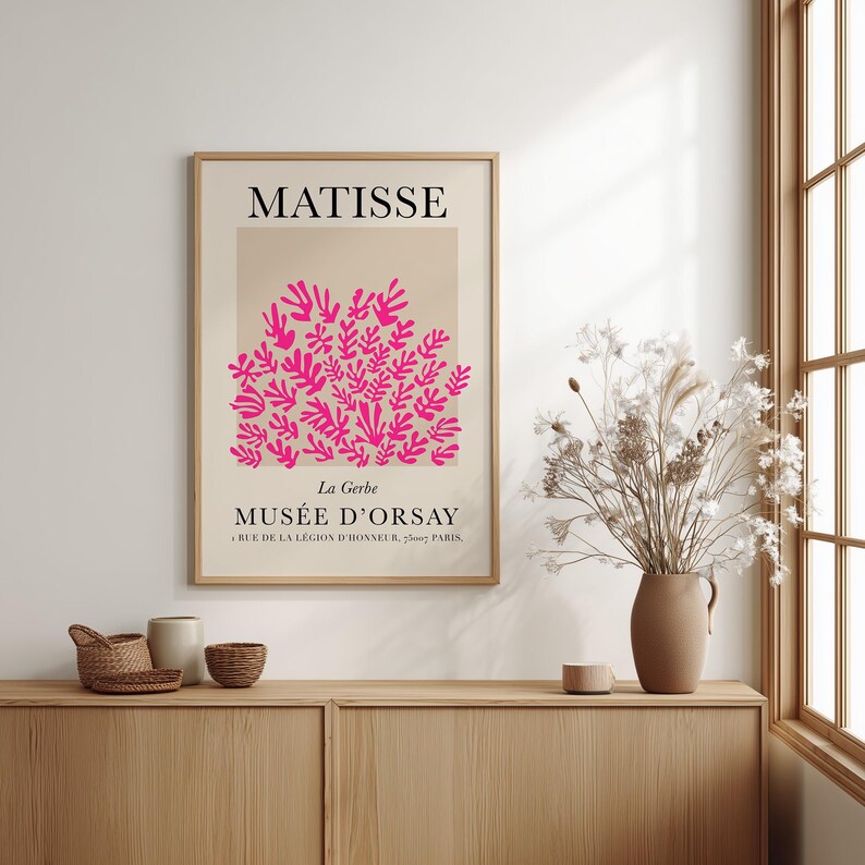 May include: A framed art print featuring a pink floral design against a beige background, with the name "MATISSE" at the top. Below, the text reads "MUS&Eacute;E D'ORSAY, Paris". The print is displayed on a wooden cabinet.