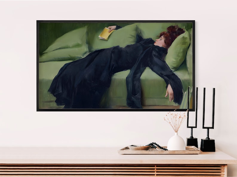 K&ouml;nnte beinhalten: Ein gerahmter Kunstdruck, der ein Gem&auml;lde einer Person mit rotbraunem Haar in einem langen schwarzen Kleid zeigt, die auf einem hellgr&uuml;nen Sofa liegt und ein kleines gelbes Buch h&auml;lt. Das Kunstwerk ist in einem d&uuml;nnen schwarzen Rahmen pr&auml;sentiert.
