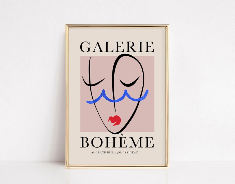 May include: A gold framed poster with a pink background and a black line drawing of a face with blue eyelashes and a red mouth. The text "GALERIE BOHEME" is in black at the top and "66 GRAND RUE, 92160 ISSY-LES-MOULINEAUX" is in black at the bottom.