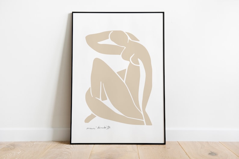 May include: A beige abstract line drawing of a person sitting with their arm raised above their head. The drawing is framed in a black frame and the text "femme - made by me" is at the bottom of the drawing.