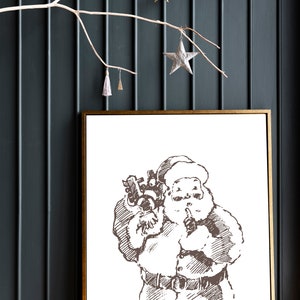 May include: A framed black and white illustration of Santa Claus holding a bag of gifts and putting a finger to his lips. The illustration is on a white background.