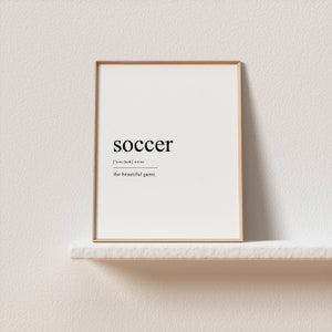 May include: A framed print with the word "soccer" in black text, with the phonetic pronunciation and the definition "the beautiful game".