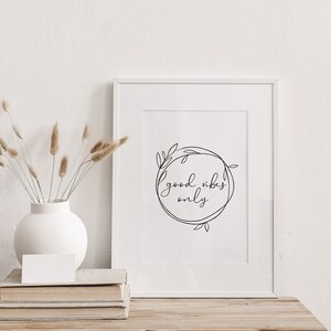 May include: White framed print with black line art of a wreath with the text "good vibes only" inside.