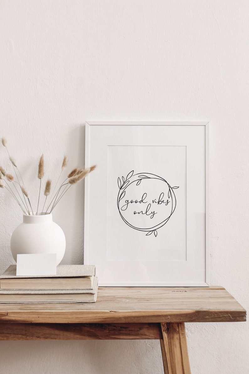 May include: White framed print with black line art of a wreath with the text "good vibes only" inside.