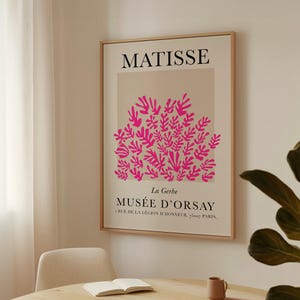 May include: A framed art print featuring a pink floral design against a beige background. The print includes the name "MATISSE" at the top and "MUS&Eacute;E D'ORSAY" at the bottom, with additional text below. The frame is a light wood color.
