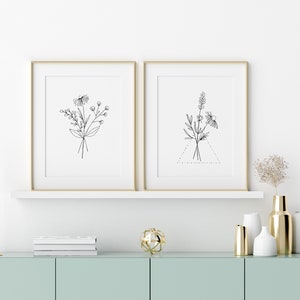 May include: Two framed black and white line drawings of floral bouquets, one with a triangle shape, on a white wall above a light blue cabinet with gold accents.
