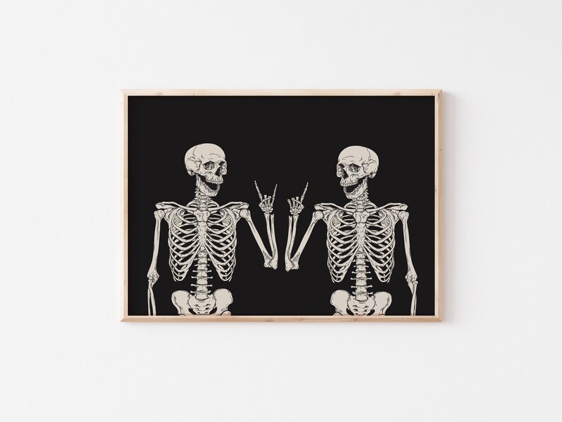 May include: A framed wall art print featuring two off-white human skeletons against a solid black background. Both skeletons are positioned facing each other, each raising one hand to make a rock and roll hand gesture with extended fingers.