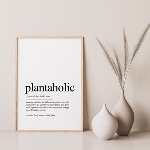Puede incluir: Una impresi&oacute;n de arte imprimible en blanco y negro con la definici&oacute;n de la palabra "plantaholic", que se define como alguien que tiene una adicci&oacute;n a las plantas. La impresi&oacute;n est&aacute; enmarcada en un marco de madera claro.