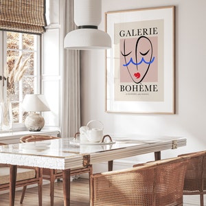 May include: A minimalist poster with a pink background and a black line drawing of a face with blue and red accents. The text "GALERIE BOHEME" is printed in black at the top and bottom of the poster.