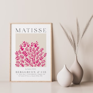 May include: A framed poster with a beige background and a pink abstract design of leaves. The poster has the text "MATISSE" at the top and "La Gerbe (1953)" and "BERGGRUEN & CIE" at the bottom.