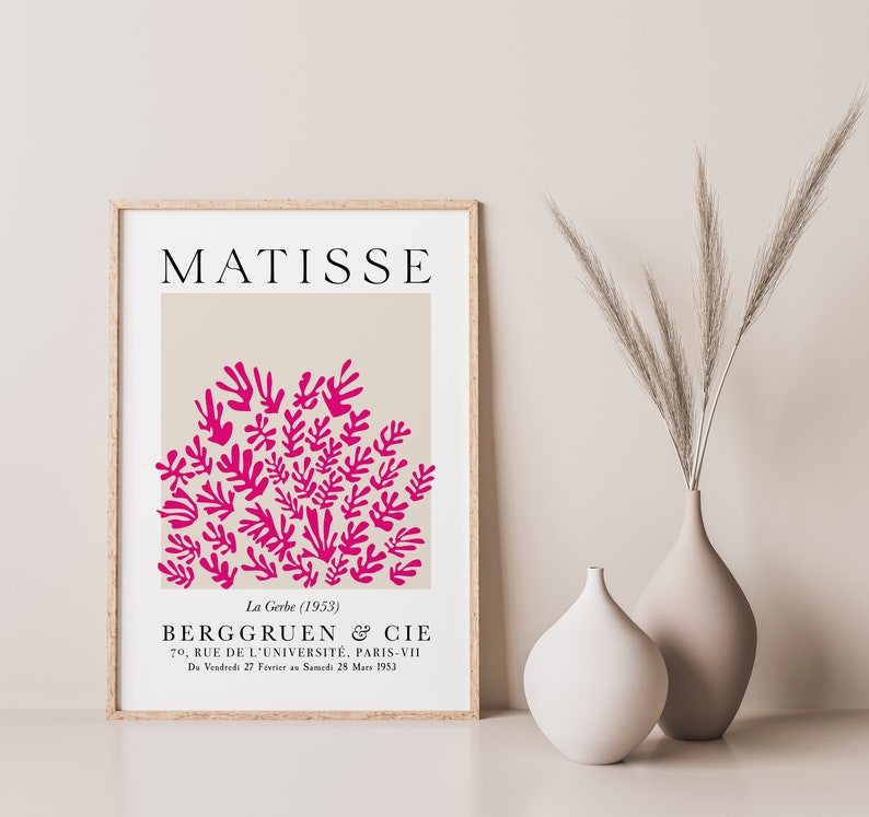 May include: A framed poster with a beige background and a pink abstract design of leaves. The poster has the text "MATISSE" at the top and "La Gerbe (1953)" and "BERGGRUEN & CIE" at the bottom.
