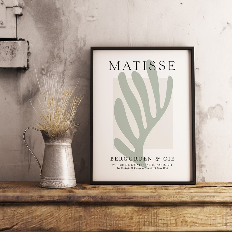 Op de afbeelding: Een zwart ingelijste print met een lichtgroen abstract bladontwerp en de tekst "MATISSE" en "BERGGRUEN & CIE" in wit. De tekst onder het ontwerp luidt "70. RUE DE L'UNIVERSIT&Eacute;, PARIS-VII" en "Du Vendredi 27 F&eacute;vrier Samedi 28 Mars 1953".