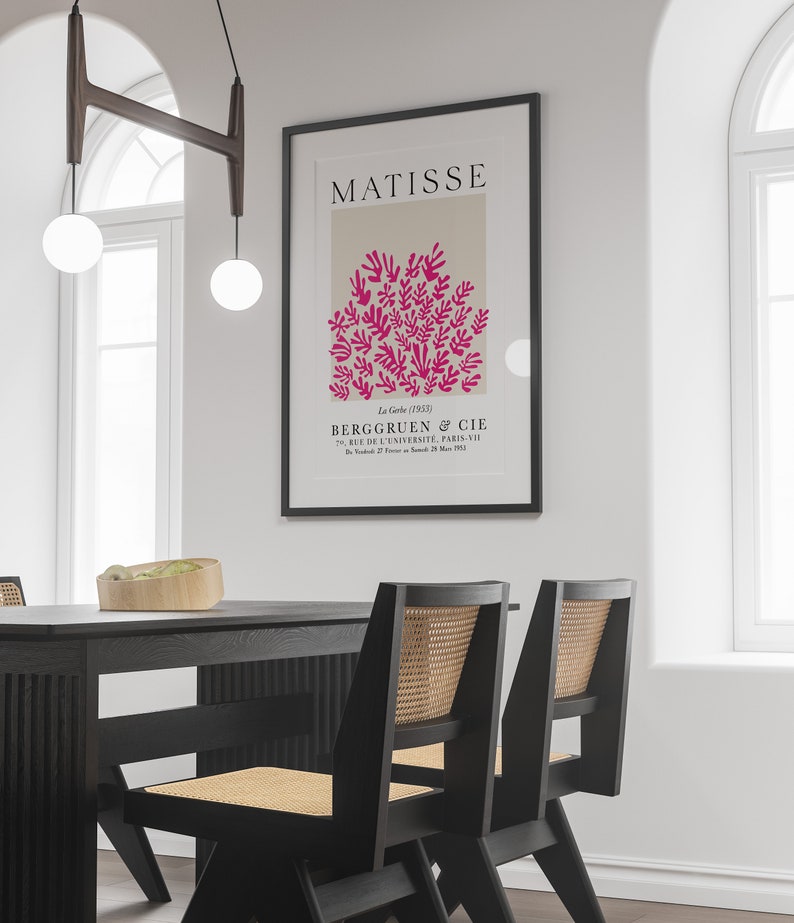 May include: A black framed poster with the text "MATISSE" in white letters. The poster features a pink abstract design of leaves and branches on a beige background. The text "La Gerbe (1953)" is in black letters below the design. The text "BERGGRUEN & CIE" is in black letters below the date. The text "70, RUE DE L'UNIVERSIT&Eacute;, PARIS-VII" is in black letters below the company name. The text "Du Samedi 27 Fevrier au Samedi 28 Mars 1953" is in black letters below the address.