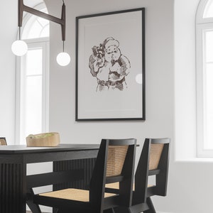 May include: A black framed print of a vintage illustration of Santa Claus holding a bag of gifts. The print is hanging on a white wall above a black dining table with two black chairs with woven cane seats.