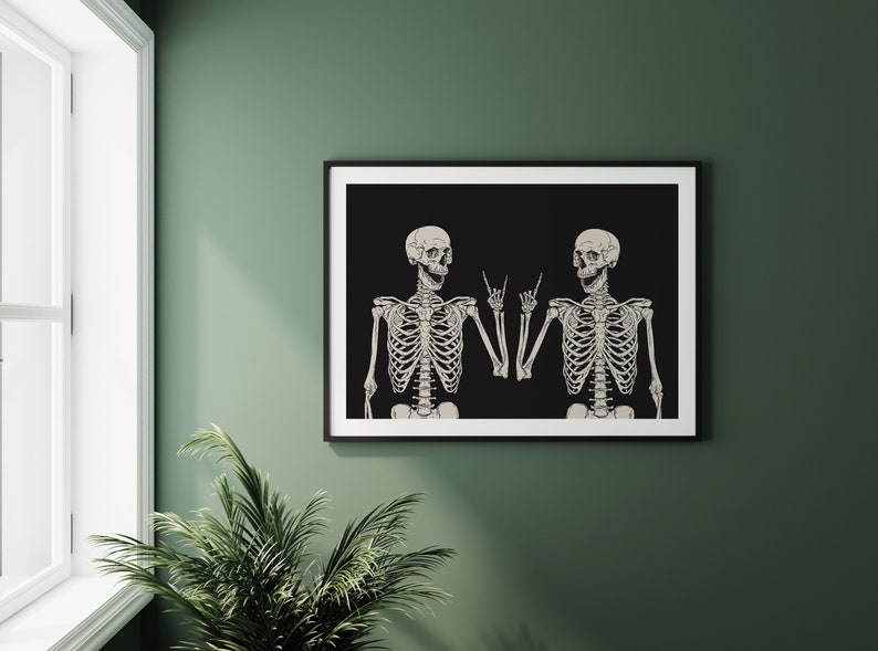 May include: A framed wall art print featuring two off-white skeletons against a solid black background. Both skeletons are depicted from the chest up, each raising one hand to make a rock and roll hand gesture with their fingers pointed upward.