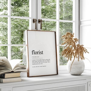 May include: A framed print with a white background and black text defining the word "florist". The text reads: "florist ['flɔːrɪst] noun a master of colour and creativity, a person with green fingers and fabulous flair, has a habit of saving the day when you're in a panic. like a normal person only cooler. see also: life saver, wizard, magician."