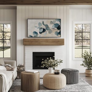 May include: A living room with a white brick fireplace, a wooden mantel, and a framed abstract painting of blue and green leaves. There are two round coffee tables, one with a woven top and one with a wooden top. A white vase with green plants sits on the woven coffee table. A black and white striped ottoman sits in the corner of the room.