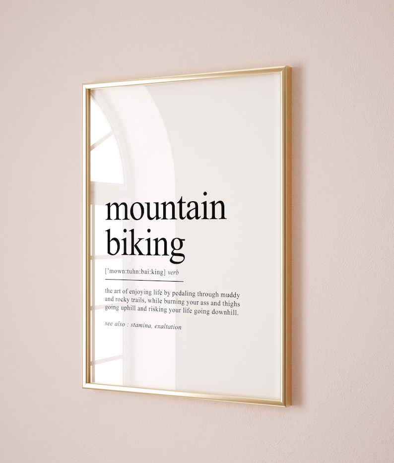 Op de afbeelding: Een zwart-wit typografische print met het woord "mountainbiken" gedefinieerd als "de kunst van genieten van het leven door te fietsen over modderige en rotsachtige paden, terwijl je je billen en dijen verbrandt tijdens het bergop fietsen en je leven riskeert tijdens het bergaf fietsen." De print bevat ook de zin "zie ook: uithoudingsvermogen, extase".