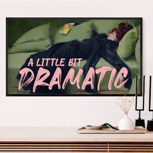 K&ouml;nnte beinhalten: Ein gerahmter Wandkunstdruck mit einem Gem&auml;lde einer Person in einem schwarzen Kleid, die auf einem gr&uuml;nen Sofa liegt und ein gelbes Buch h&auml;lt. Der Text A LITTLE BIT DRAMATIC ist in gro&szlig;en, hellrosa Pinselbuchstaben mittig &uuml;berlagert.
