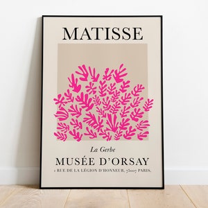 May include: A framed art print featuring the name "MATISSE" at the top. Below, a beige rectangle contains a cluster of bright pink leaf-like shapes. The text "MUS&Eacute;E D'ORSAY" and address are at the bottom. The print is displayed on a white wall.