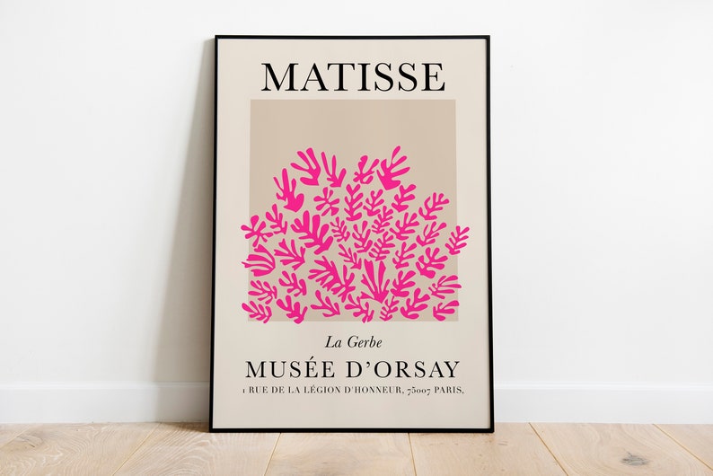 May include: A framed art print featuring the name "MATISSE" at the top. Below, a beige rectangle contains a cluster of bright pink leaf-like shapes. The text "MUS&Eacute;E D'ORSAY" and address are at the bottom. The print is displayed on a white wall.