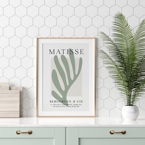 Op de afbeelding: Een ingelijste print van een Matisse-schilderij met een abstract bladontwerp in groen op een beige achtergrond. De print bevat de naam van de kunstenaar, "MATISSE", en de galerie-informatie: "BERGGRUEN & CIE, 70. RUE DE L'UNIVERSIT&Eacute;, PARIS-VII, D2728 M 1952."