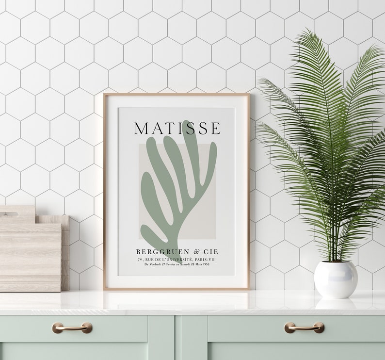 Op de afbeelding: Een ingelijste print van een Matisse-schilderij met een abstract bladontwerp in groen op een beige achtergrond. De print bevat de naam van de kunstenaar, "MATISSE", en de galerie-informatie: "BERGGRUEN & CIE, 70. RUE DE L'UNIVERSIT&Eacute;, PARIS-VII, D2728 M 1952."