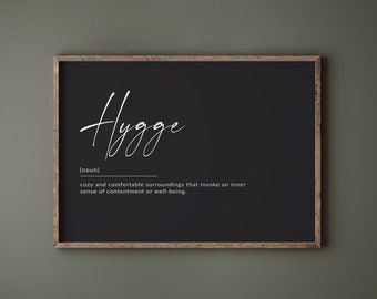 Könnte beinhalten: Schwarz gerahmter Druck mit dem Wort "Hygge" in weißer Kursivschrift. Die Definition von Hygge lautet: "Gemütliche und komfortable Umgebung, die ein inneres Gefühl von Zufriedenheit oder Wohlbefinden hervorruft."