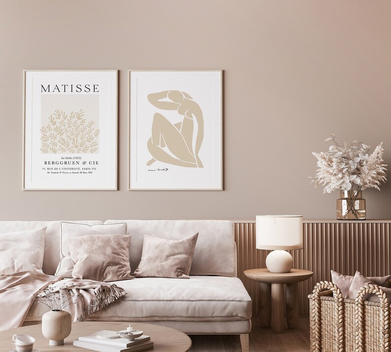 May include: Two framed art prints on a beige wall. The print on the left features a floral design with the text "MATISSE" and "BERGGRUEN & CIE". The print on the right features a nude figure in a minimalist style.