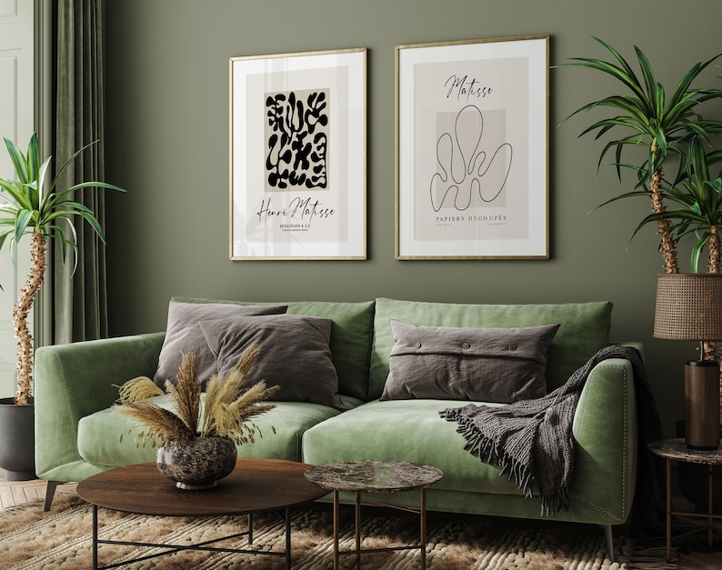 K&ouml;nnte beinhalten: Zwei gerahmte Kunstdrucke mit einem gr&uuml;nen Samtsofa, einer Topfpflanze und einem Couchtisch im Vordergrund. Die Drucke zeigen abstrakte Designs in Schwarzwei&szlig; mit dem Text "Henri Matisse" und "Matisse Papiers Decoupes".