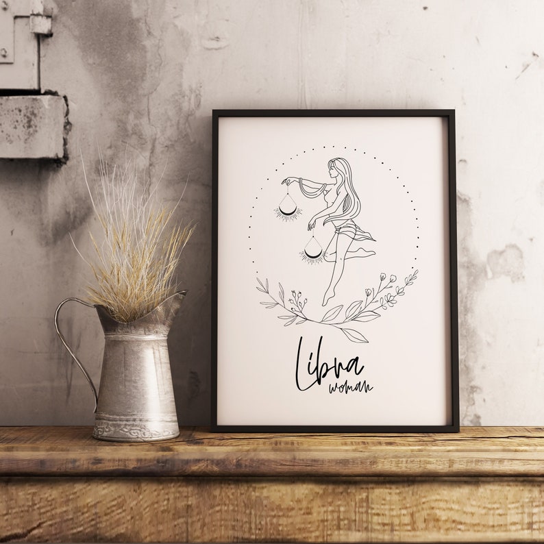 May include: Black and white line art print of a Libra woman with a scale and floral accents. The print is framed in a black frame and has the text "Libra woman" at the bottom.