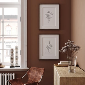 May include: Two framed black and white line drawings of flowers on a brown wall. The drawings are in simple, minimalist style. A brown leather chair sits in the corner of the room.