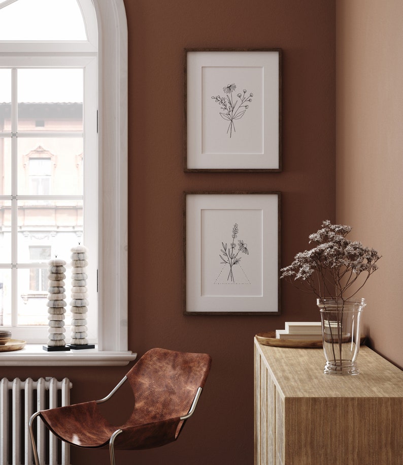 May include: Two framed black and white line drawings of flowers on a brown wall. The drawings are in simple, minimalist style. A brown leather chair sits in the corner of the room.