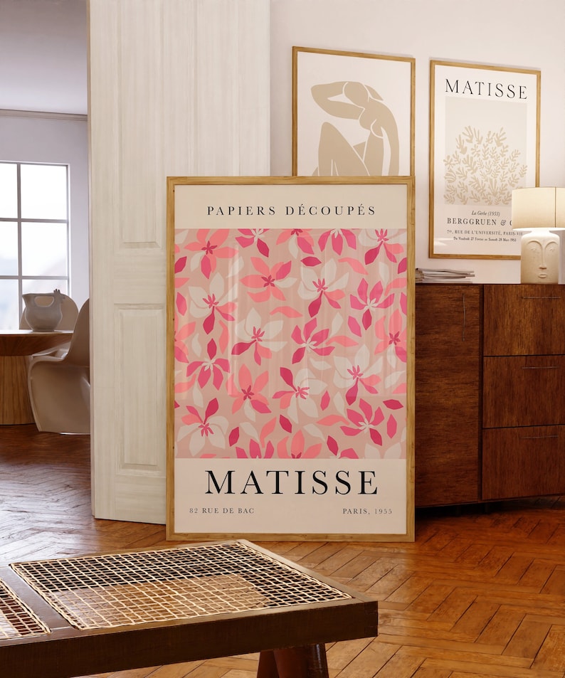 May include: A framed print of a pink and white floral pattern with the text "PAPIERS D&Eacute;COUP&Eacute;S" and "MATISSE" in black. The print also includes the text "82 RUE DE BAG" and "PARIS, 1953" in black.