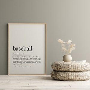 May include: A framed print with a minimalist design featuring the word "baseball" and its definition. The definition describes the game as played with a bat, ball, and gloves between two teams of nine players on a field with four white bases. The print is set against a light green wall with a vase of dried pampas grass on a woven stool.