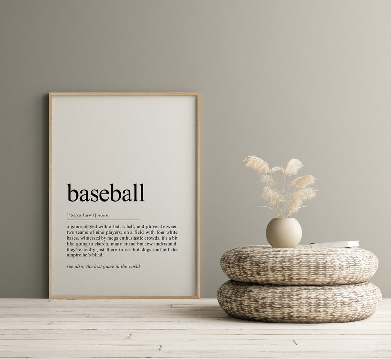 May include: A framed print with a minimalist design featuring the word "baseball" and its definition. The definition describes the game as played with a bat, ball, and gloves between two teams of nine players on a field with four white bases. The print is set against a light green wall with a vase of dried pampas grass on a woven stool.