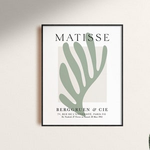 Op de afbeelding: Een zwart ingelijste poster met een witte achtergrond en een groen abstract bladontwerp. De tekst "MATISSE" staat bovenaan de poster. De tekst "BERGGRUEN & CIE" staat onderaan de poster, samen met het adres "70, RUE DE L'UNIVERSIT&Eacute;, PARIS-VII" en de datum "D2725 M 1953".