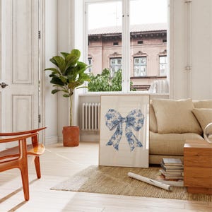 Puede incluir: Una impresi&oacute;n enmarcada de un lazo con estampado floral azul y blanco sobre fondo blanco. La impresi&oacute;n est&aacute; colgada en una pared blanca en un sal&oacute;n.