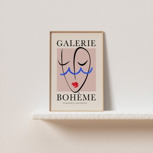 May include: A framed poster with a pink background and a black line drawing of a face with blue wavy lines above the eyes and a red mouth. The text "GALERIE BOHEME" is in black at the top and bottom of the poster. The address "46 GRAND RUE, 92200 ISSY-LES-MOULINEAUX" is in black at the bottom of the poster.