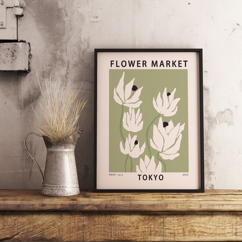 以下が含まれることがあります： 緑色の背景に白いスタイリッシュな花が描かれた額装されたプリント。プリントの上部には「FLOWER MARKET」、下部には「TOKYO」の文字が書かれている。